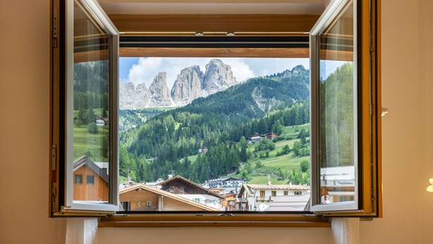 Une fenêtre donnant sur un paysage montagneux, avec une maison et un sommet de montagne en vue.