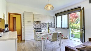 A modern kitchen with white cabinets, a dining table with floral tablecloth, and a large window with a view of a garden.