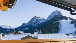 A wooden deck overlooking a mountainous landscape with snow-covered peaks and a ski slope. - Apartment Deluca by Interhome (Pozza di Fassa)