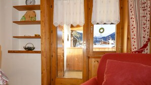 A cozy room with wooden walls, a red sofa, and a view of mountains through a window. - Apartment Deluca by Interhome (Pozza di Fassa)