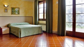 Ein Schlafzimmer mit Bett, Nachttisch, Wandlampe, Fenster mit Vorhängen und einer Tür.