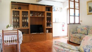 Een woonkamer met een houten kast, een televisie, een bloemenbank en een eettafel met stoelen.