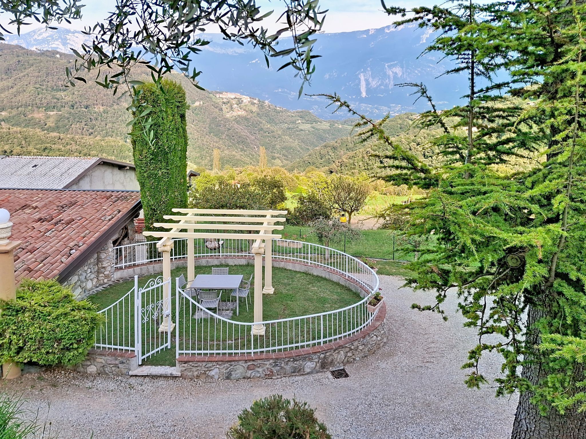 Un jardin agrémenté d’une pergola, d’un chemin de gravier et offrant une vue sur un paysage montagneux.