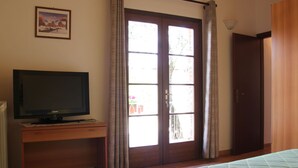 Ein Schlafzimmer mit einem Bett, einem Fernseher auf einem Holztisch, einer Tür und einem Fenster mit Vorhängen.