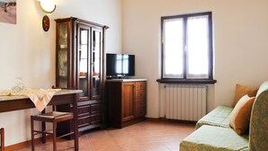 Ein kompakter Wohnraum mit einem Holzkasten, einem Fernseher, einem Fenster mit Jalousien, einer Heizung und einem gemusterten Sofa.