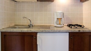 Une cuisine avec des meubles en bois, un crédence en carrelage blanc, un évier en acier inoxydable, une machine à café blanche et une cuisinière à gaz.