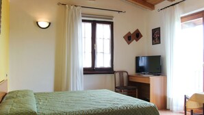 Une chambre à coucher avec un lit, un bureau avec une télévision, une chaise et une fenêtre avec des rideaux.