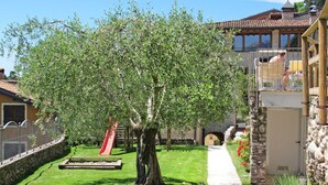 Un patio soleado con un árbol grande, un tobogán rojo y un camino de piedra que lleva a un edificio con balcón.