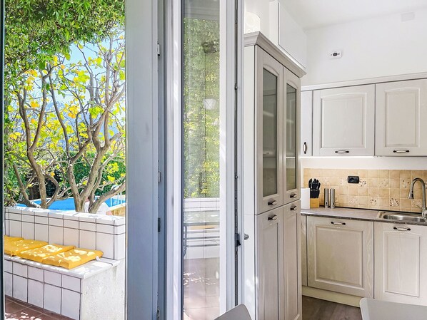 A modern kitchen with white cabinets, a built-in oven, and a view of trees outside.