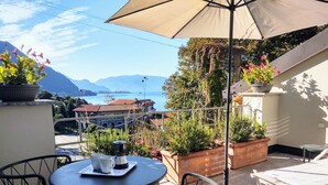 A terrace with a table and chairs, potted plants, and a view of mountains and a lake.