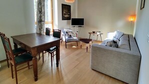 A spacious living area with a wooden dining table, two chairs, a sofa, and a TV.