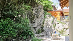 An outdoor patio with a table set for two, surrounded by greenery and a rocky backdrop. - Federico by Interhome (Dorio)