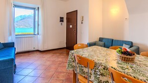 A dining area with a table set for two, a sofa, and a view of the sea through a window. - Vecchia Filanda (MSO150) Apartment 302 by Interhome (Musso)