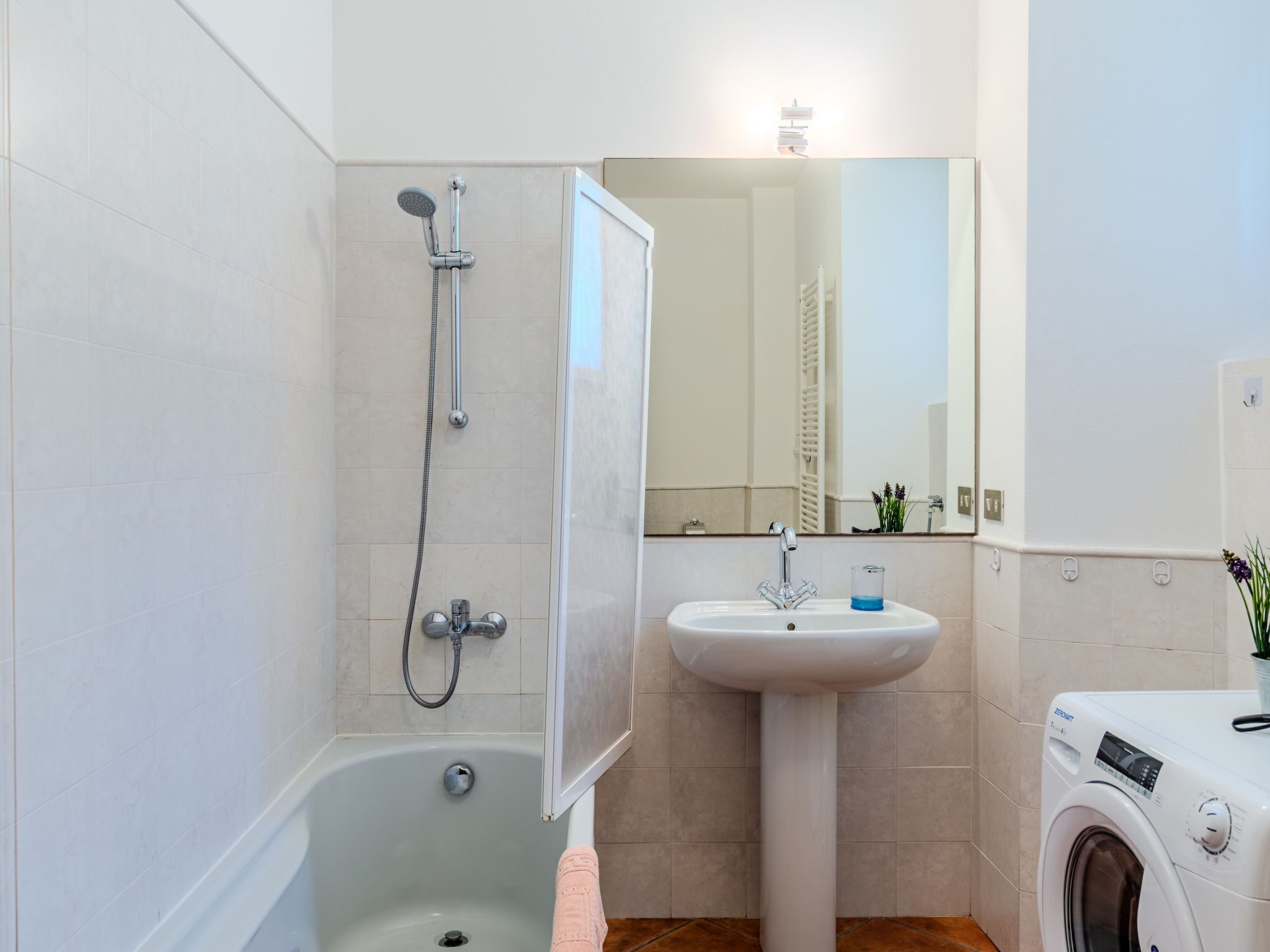 A bathroom with a bathtub, a sink, a mirror, and a washing machine.