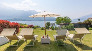 Eine Terrasse mit vier Liegestühlen und einem Tisch, mit Blick auf einen See und Berge im Hintergrund.