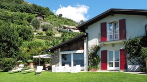 Ein zweistöckiges Haus mit Balkon, umgeben von üppiger Vegetation und einer Hügelslandschaft.