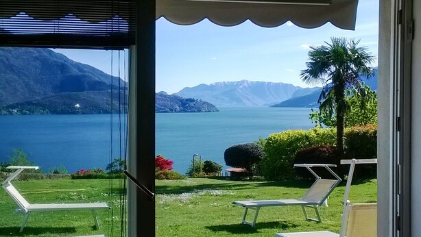 Ein Balkon mit Blick auf einen See und Berge, zwei Liegestühle und ein kleiner Tisch.
