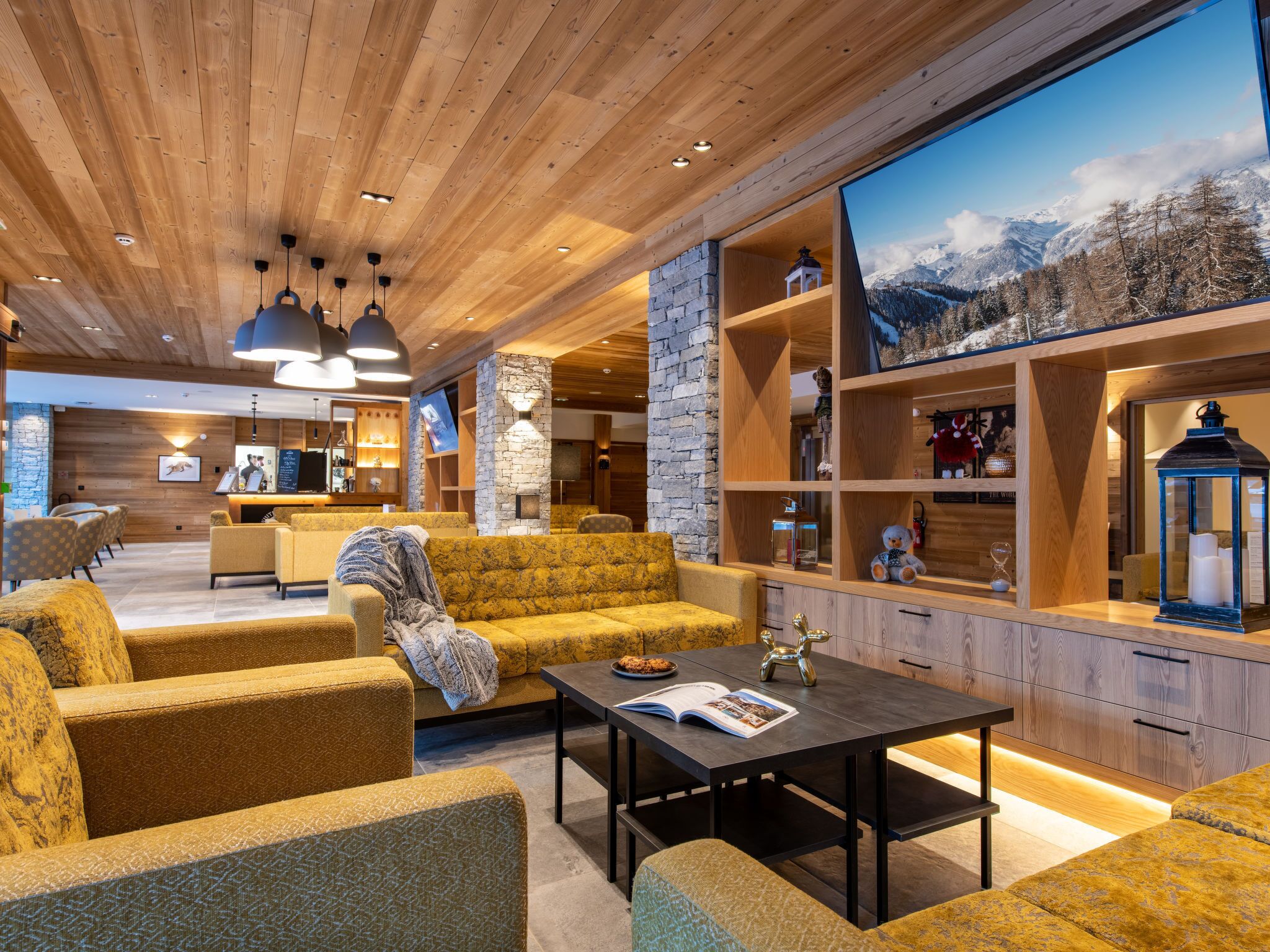 Ein modernes Interieur mit Holzbalkendecken, einer Wand aus Naturstein und einem großen Fenster mit Blick auf die Berge.