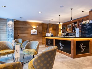 Uma área de bar com paredes de madeira, uma parede de destaque em pedra e um quadro de menu. Há banquetas e um balcão com um logotipo.