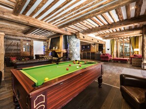 A cozy indoor setting with a pool table, leather sofas, and a stone fireplace.
