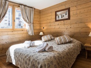 A cozy wooden room with a bed, a framed picture on the wall, and a window with curtains.