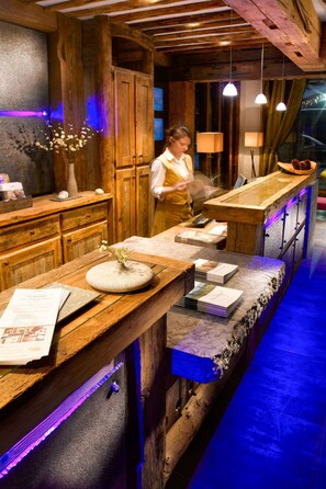 A wooden bar area with a woman working at the counter, a vase with flowers, and a menu on the table.