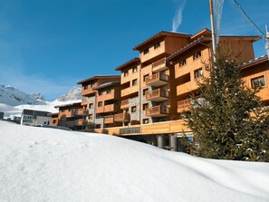 A multi-story hotel with wooden balconies and stone accents, set against a snowy mountain backdrop.