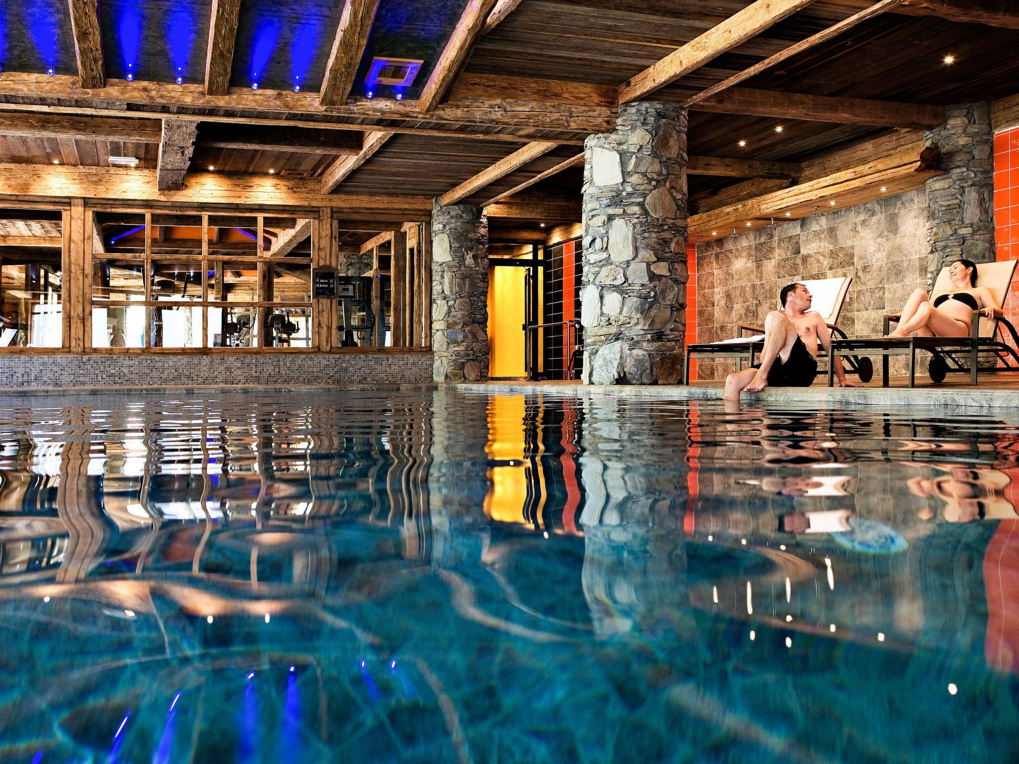 Una piscina interna con pilastri in pietra, travi di legno e un'area bar con posti a sedere.