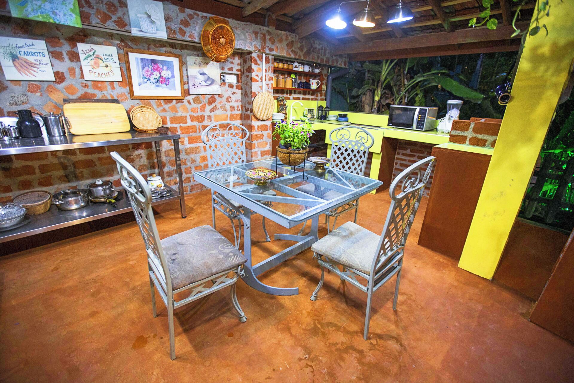 A rustic kitchen with a brick wall, a glass table, metal chairs, and various kitchen items.