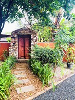 Una entrada de piedra con puerta de madera, rodeada de abundante vegetación y un camino de grava.