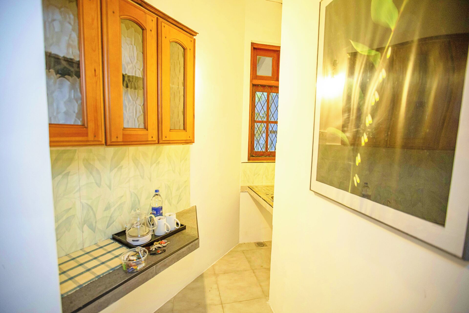 A narrow kitchen with wooden cabinets, a window with a metal grid, and a countertop with a water bottle and a coffee maker.