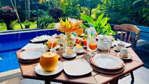 Mesa lista para el desayuno con vista a una piscina y exuberante vegetación.