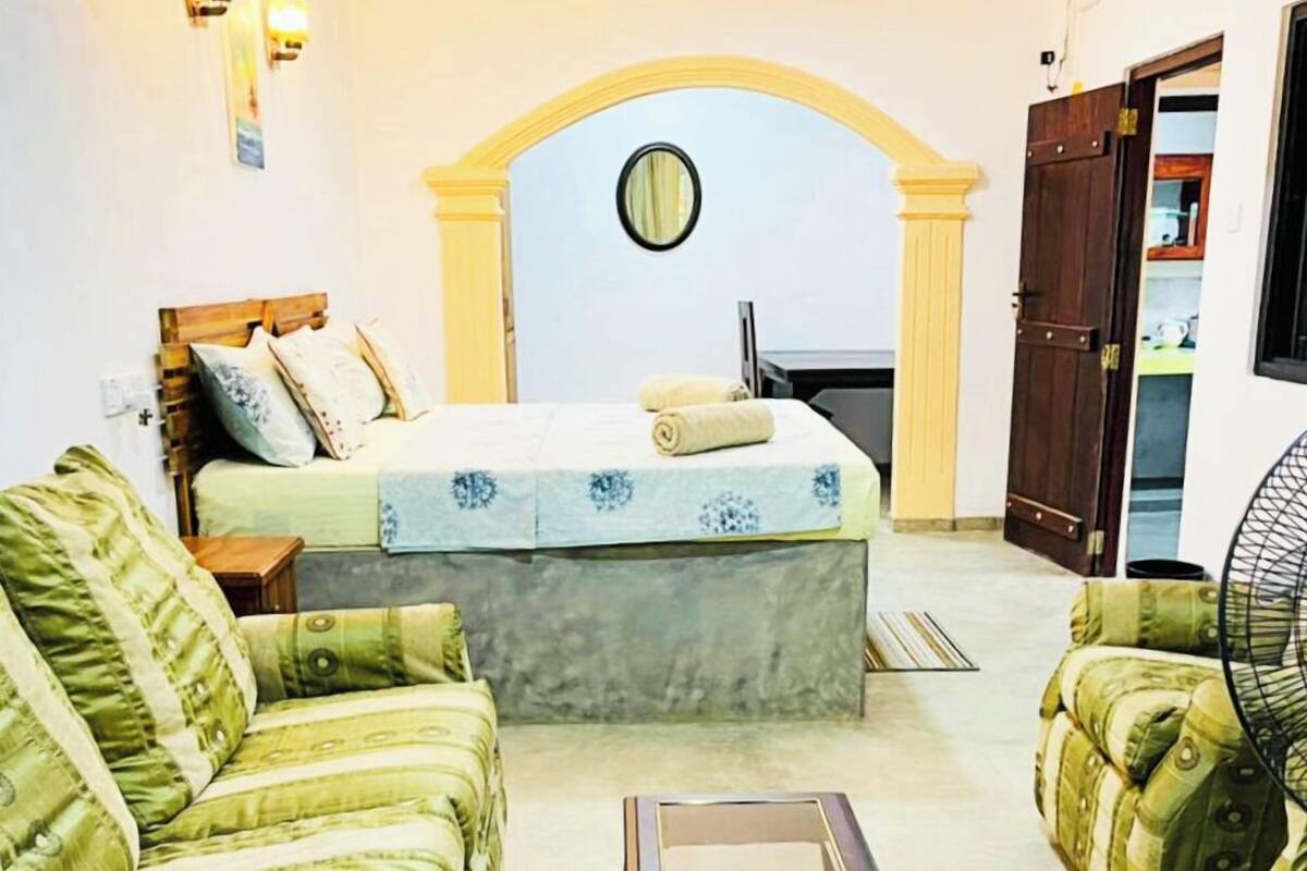 A bedroom with a bed, two sofas, a small table, and a fan.