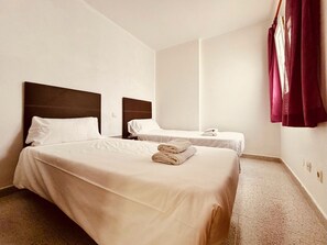Une chambre d’hôtel avec deux lits, chacun doté d’une tête de lit en bois, de draps blancs et d’une serviette pliée posée sur le lit.