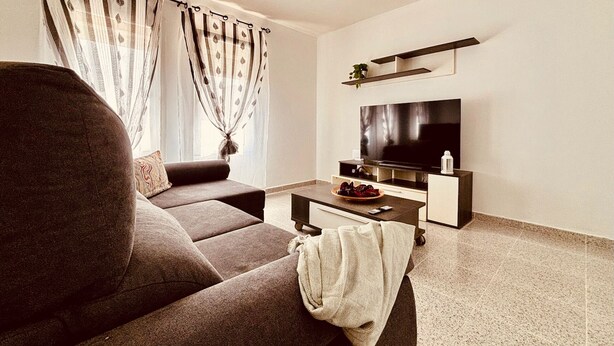 Una sala moderna con un sofá, una mesa de centro, un televisor y una estantería con una planta.