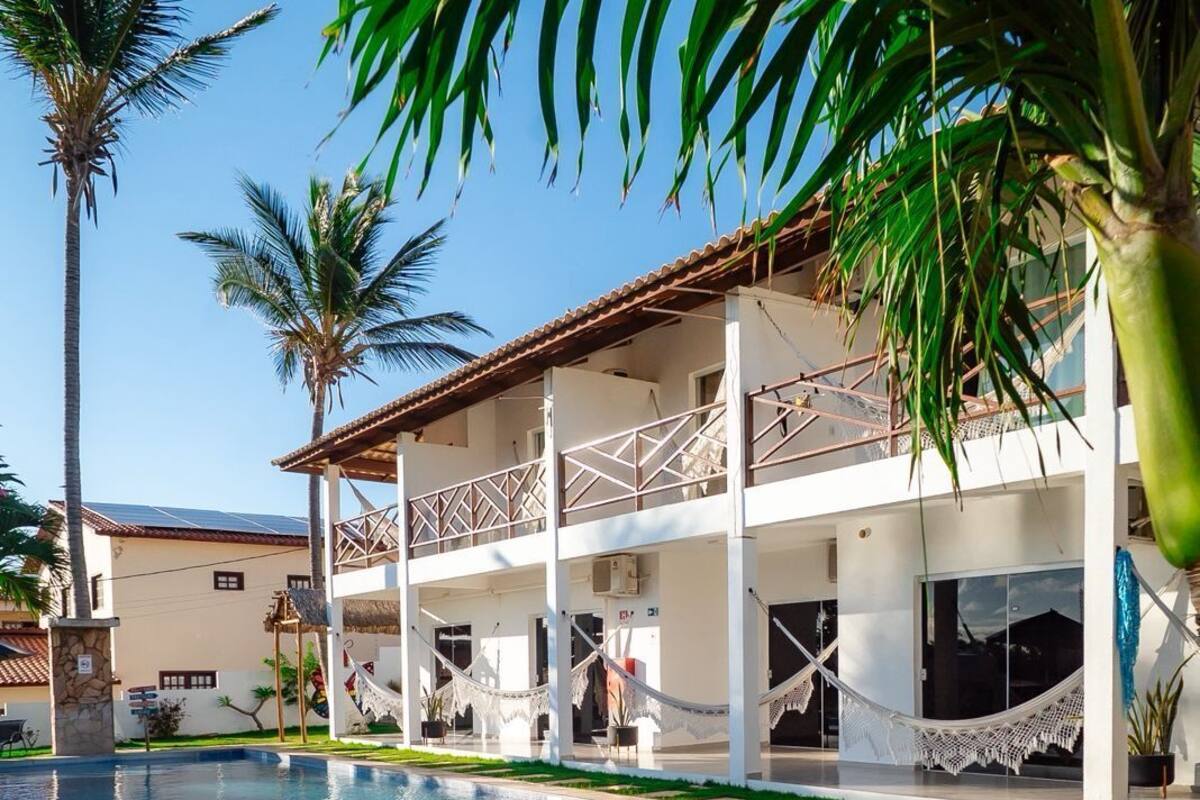 Un área de piscina con una piscina azul cristalina, un edificio blanco con balcones y palmeras.