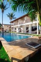 A pool area with a clear blue pool, a white building with balconies, and palm trees.