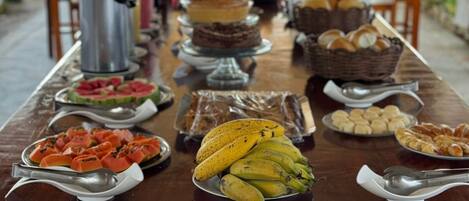 A buffet table with various fruits, pastries, and bread.