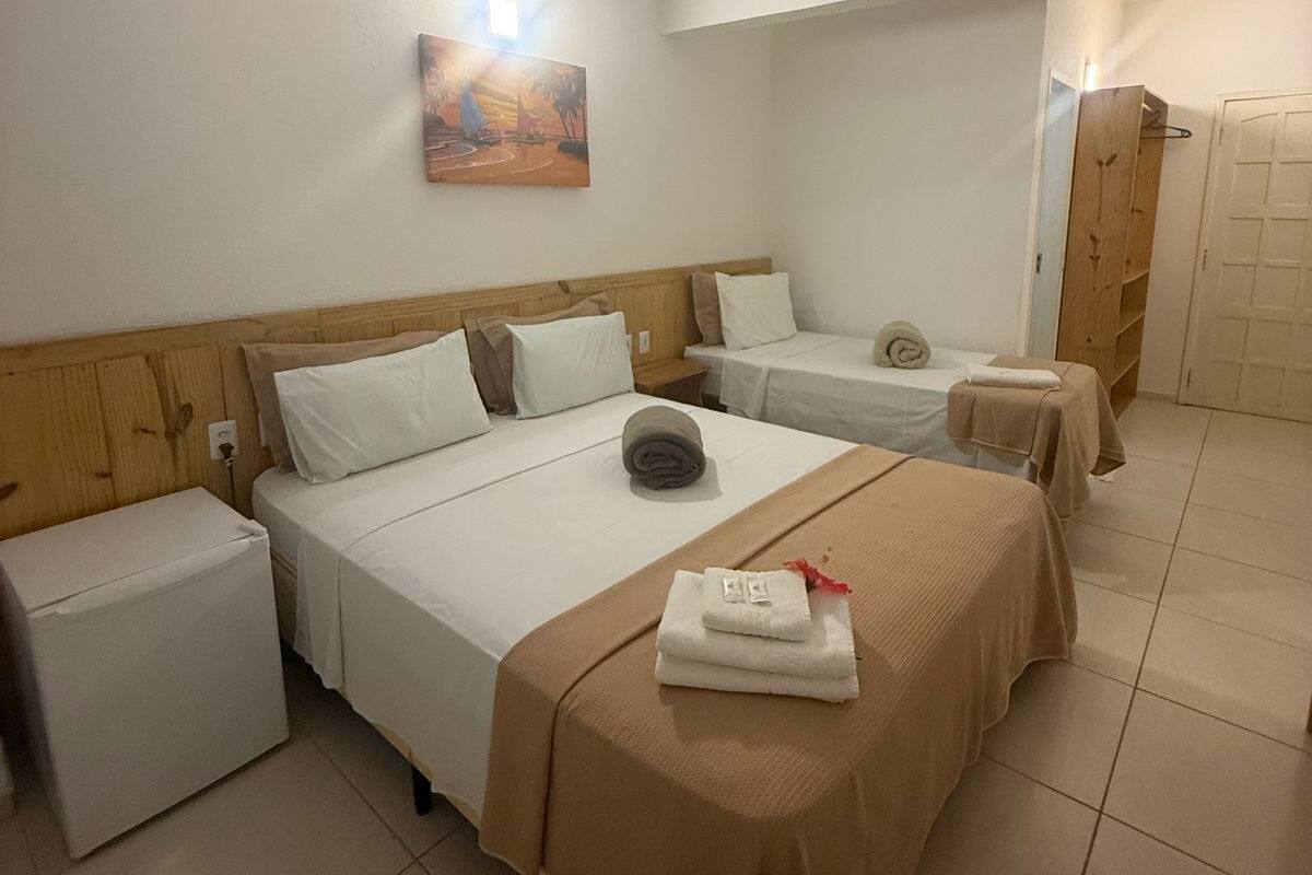 Habitación de hotel con una cama grande, dos camas más pequeñas, un cabecero de madera, un cuadro en la pared y una puerta a la derecha.