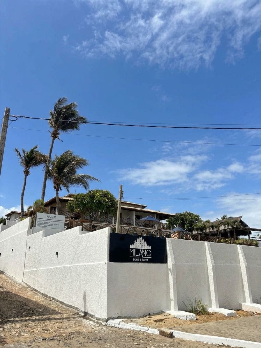 A hotel named 'MILANO' with a signboard, palm trees, and a clear sky.