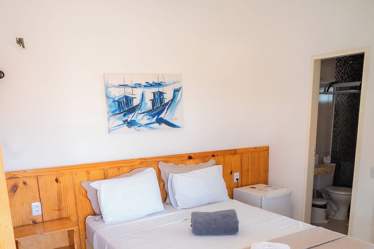 A neatly made bed with white linens, a wooden headboard, and a painting of boats on the wall.