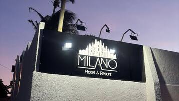 Une enseigne pour l'hôtel et le complexe de loisirs Milano, avec un mur à texture et un palmier en arrière-plan.