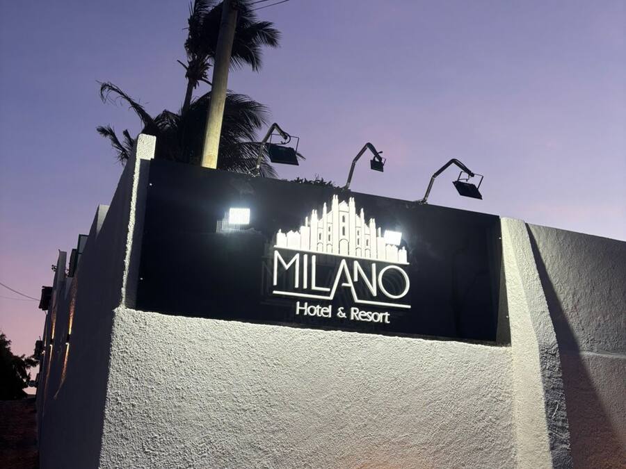 Une enseigne pour l'hôtel et le complexe de loisirs Milano, avec un mur à texture et un palmier en arrière-plan.