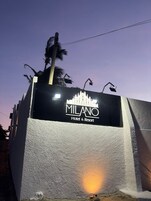 A sign for Milano Hotel & Resort with a textured wall and a palm tree in the background.