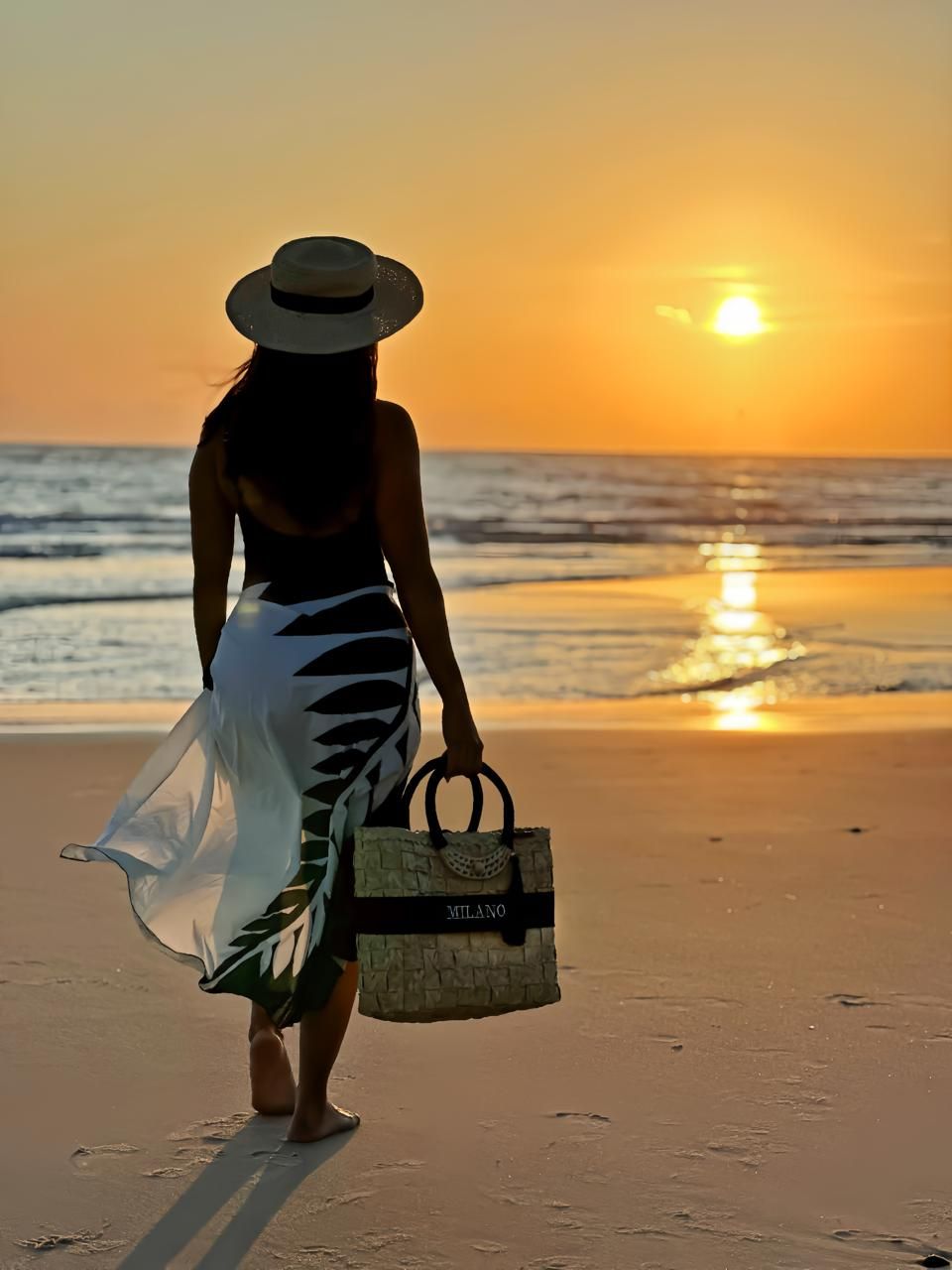 Una persona caminando por la playa con un atardecer de fondo.