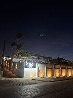 A hotel entrance at night with illuminated signage, palm trees, and a paved pathway.