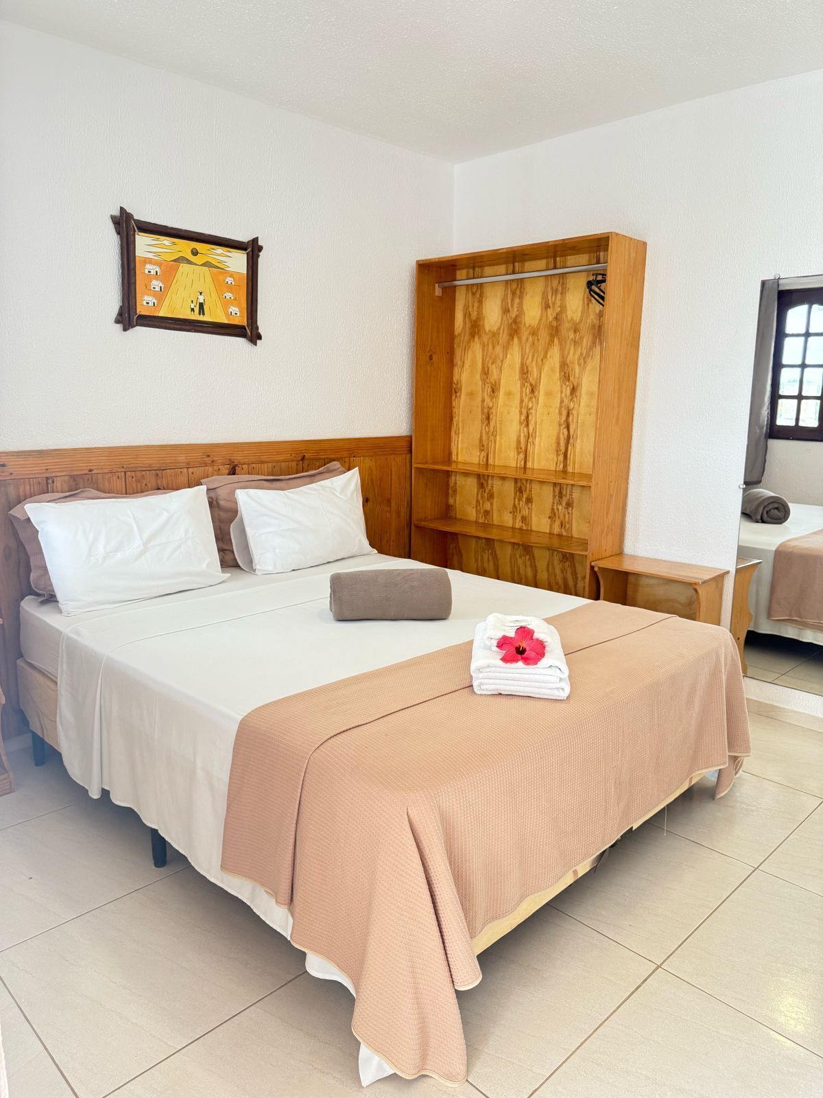 A neatly made bed with a brown blanket, a wooden wardrobe, and a framed picture on the wall.