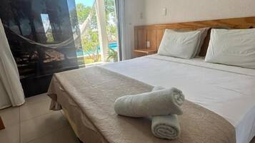 A hotel room with a bed, a wooden headboard, a large window with a view of palm trees, and a framed picture on the wall.
