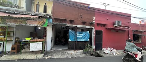 A street scene with a fruit shop displaying fresh produce and a blue banner advertising a cost-effective service.