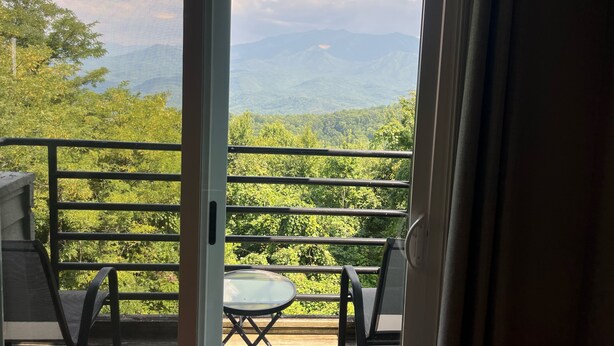 Ein Balkon mit Tisch und Stühlen, mit Blick auf eine Berglandschaft mit Bäumen.